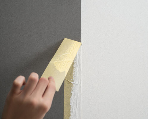 Hand taking masking tape off after painting, displaying the difference between different paint sheen levels